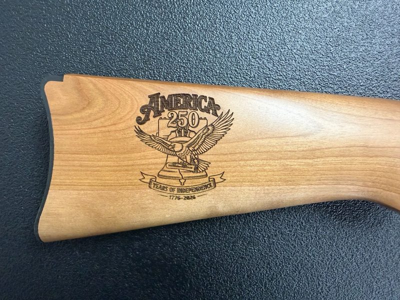 Wood rifle stock laser-engraved with an America 250 design — eagle, Liberty Bell, Years of Independence 1776–2026 — custom firearm engraving Sussex NJ